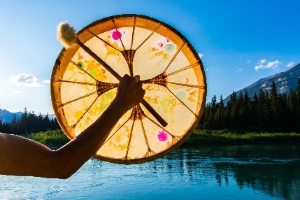 Close-up of a person's arm holding a native drum, with a nature background